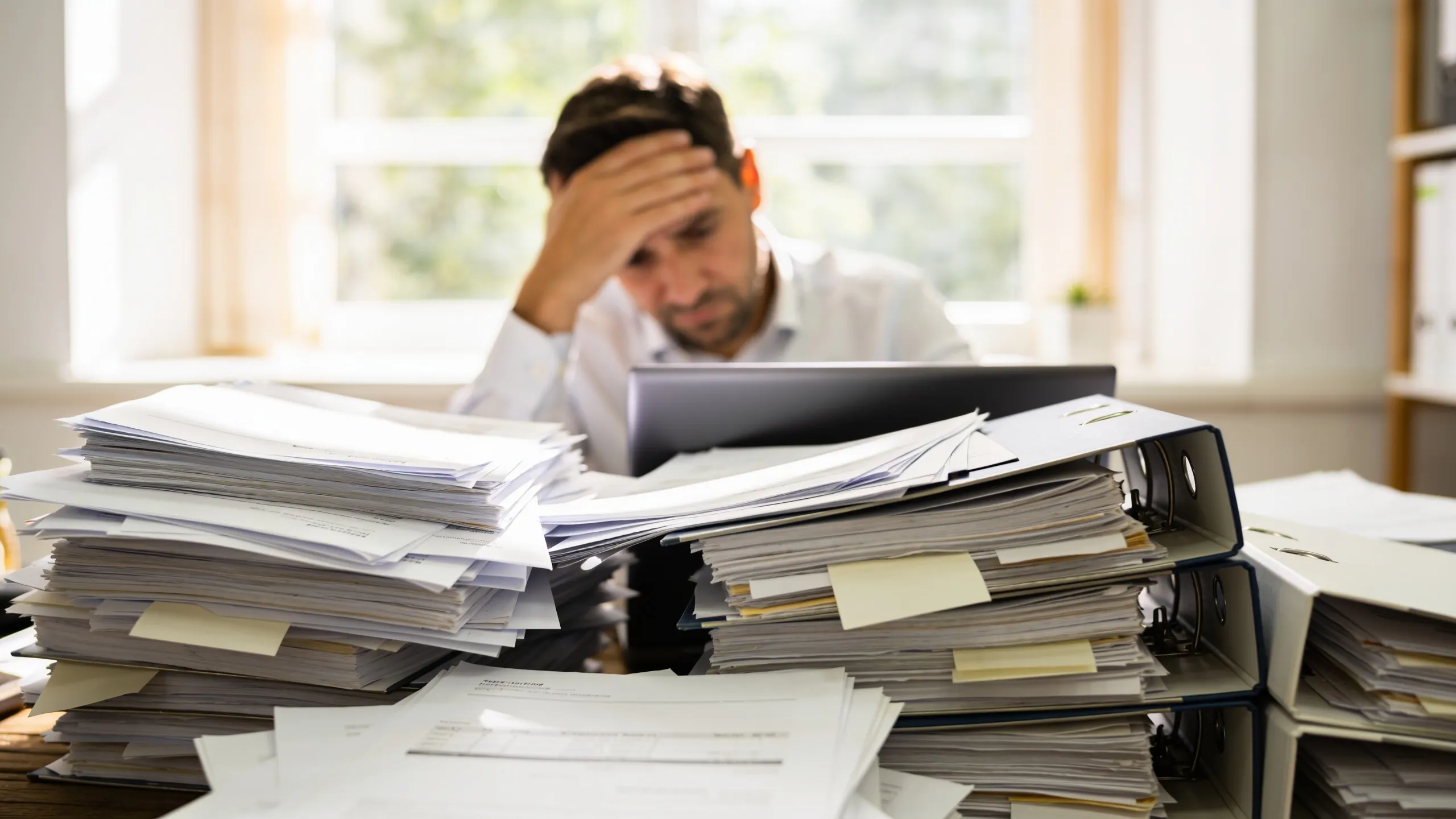 An overwhelmed small business owner at a desk behind tall stacks of paper and binders